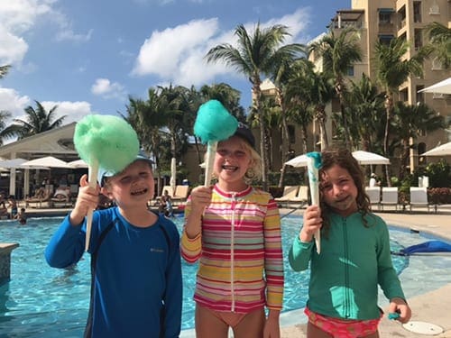 Three kids enjoy cotton candy on a sunny, tropical day.