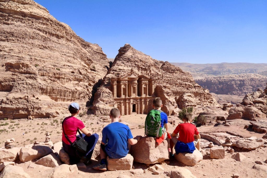 Four kids sitting on rocks look at the Monastery at Petra in Jordan.