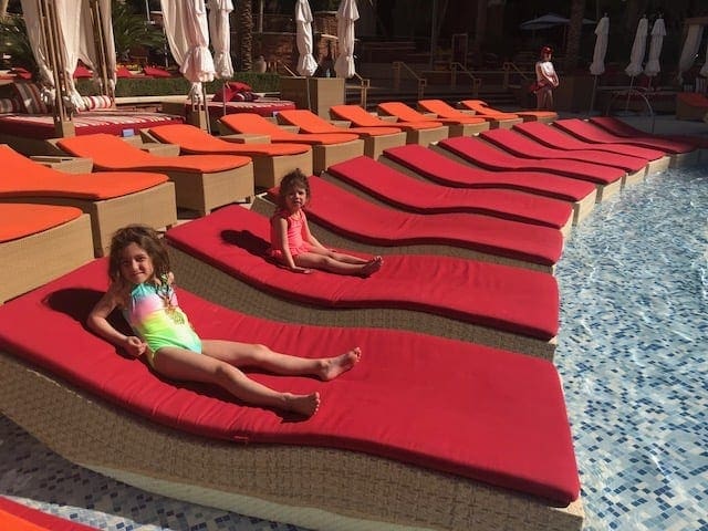 Two young girls sit on their own red, poolside loungers at Red Rock Casino Resort and Spa.