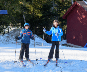 Two kids stand on cross-country ski, while exploring the Maine Hut Trails.