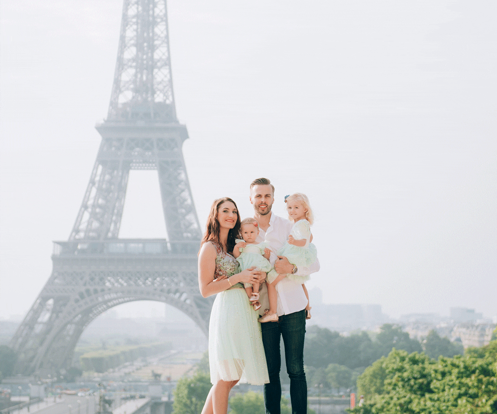 A family of four poses together with the Eiffel Tower in the distance.