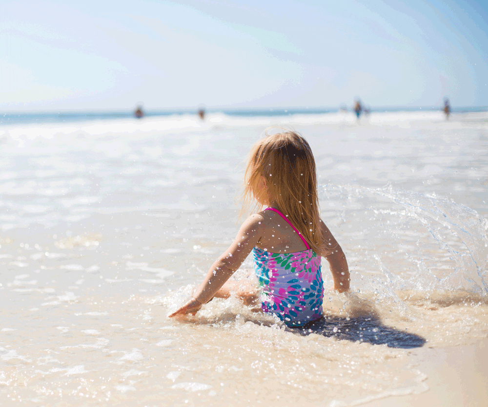 Toddler girl sitting on shore on a beach vacation