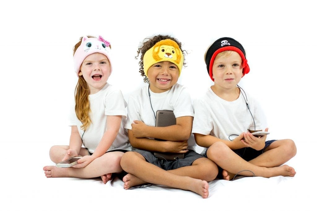Three kids sit together sporting CozyPhones headphones in the theme of a kitty, lion, and pirate, respectively.