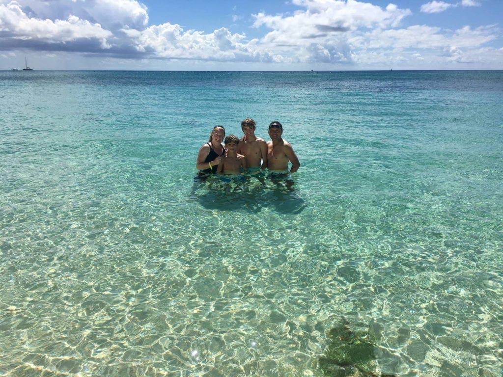 A family of four stands smiling in the water off the coast of the Seven Mile Beach in Grand Cayman.