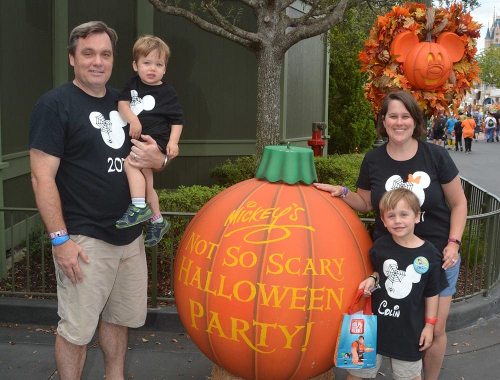 A family of four stands arond a large pumpkin at Walt Disney World, reading "Mickey's Not So Scary Halloween Party".