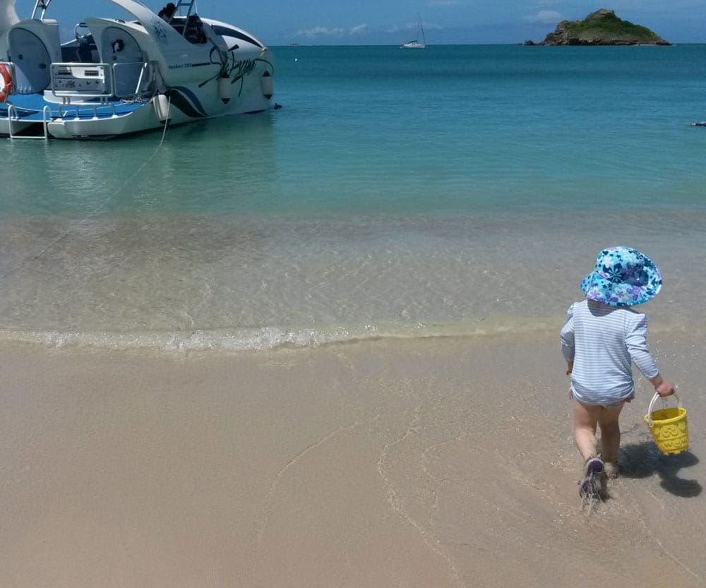 Toddler wtih blue hat and sand bucket on beach in Antigua