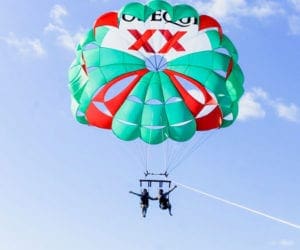 Two people parasailing with a green and red parachute on a bright sunny day in Cancun.