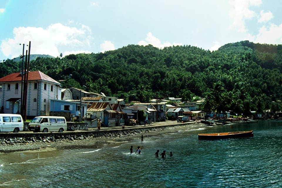 A view of Soufriere from the ocean, featuring several neighborhood buildings and boats.