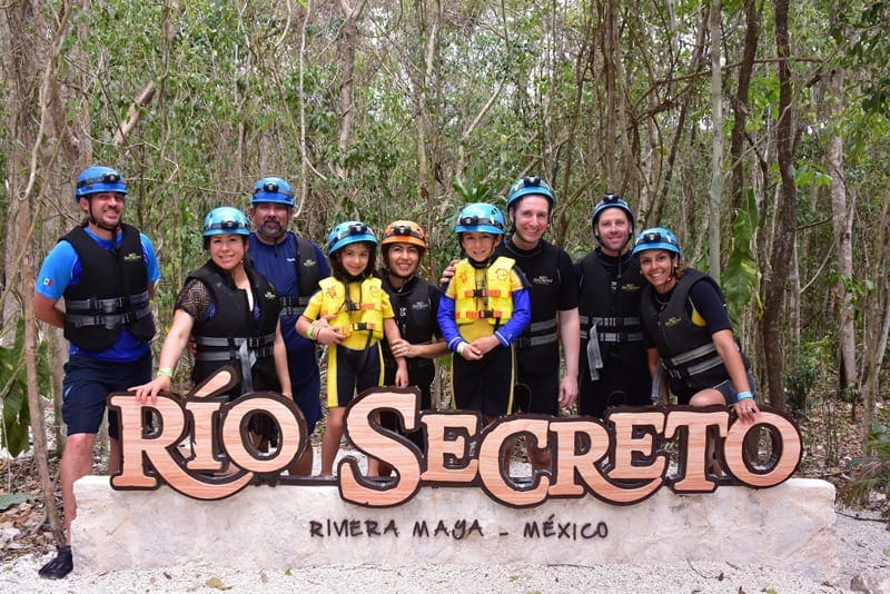 A group shot with several families in front of the Rio Secreto Mexico sign, as part of a tour.
