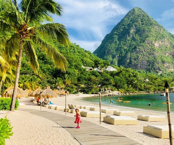 Toddler girl on the beach in St Lucia with palm trees and lounge beds
