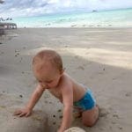 Baby in swim diaper playing in sand on beach in Antigua