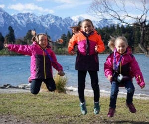 Three girls in pink jackets jumping up in New Zealand