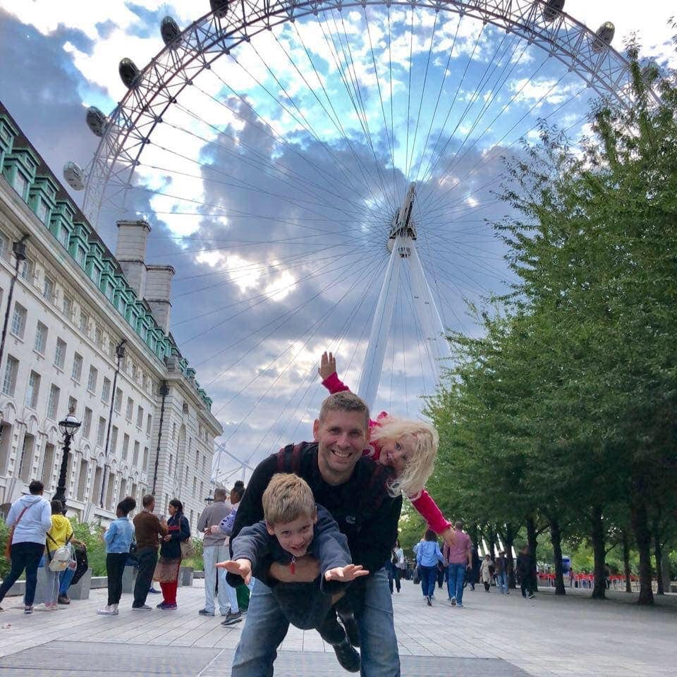 Family of three stands in front of the London eye, one of the stops on our virtual travel from home to London.