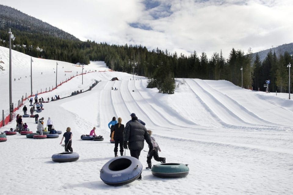 A family pulls a number of snowtubes behind them up the hill at Coca Cola Tube Park, offering some of the best Colorado snow tubing for families.