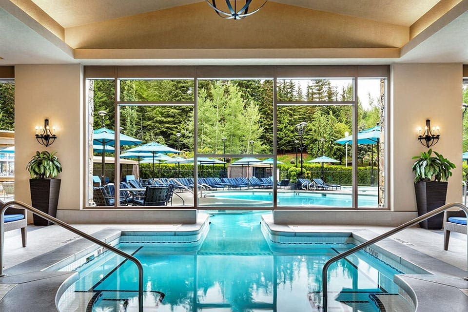 Inside the Photo Courtesy: Hotel Fairmont Château Whistler, featuring a beautiful pool with a wall full of windows behind it.