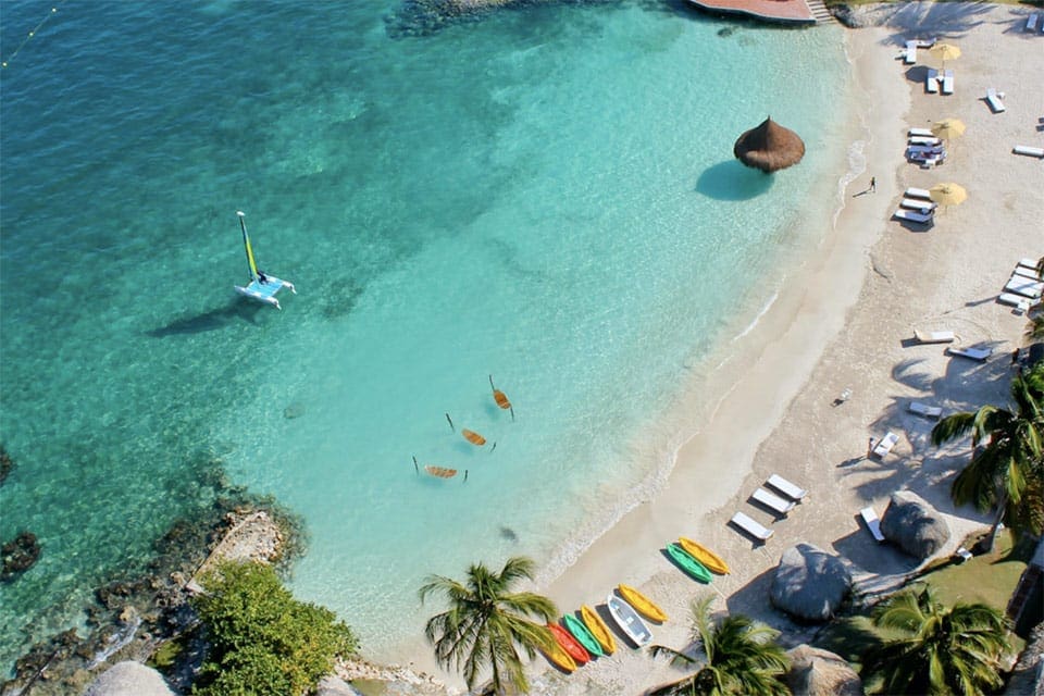 An aerial view of the beach at Hotel Punta Faro, featuring several boats in the water and resting on shore.