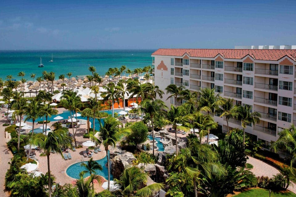 An aerial view of Aruba Marriott Ocean Club, featuring palm trees, large buildings, and a pool at one of the best Marriott Resorts in the Caribbean for families.