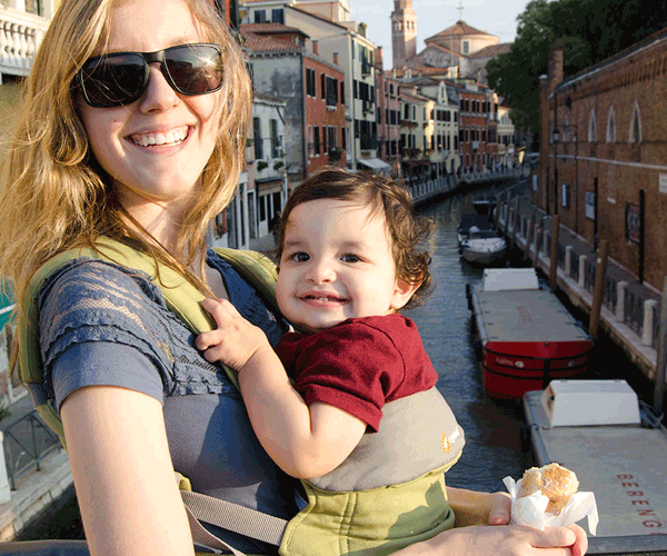 A mom holds her young baby in a baby carrier on her chest while exploring Venice.