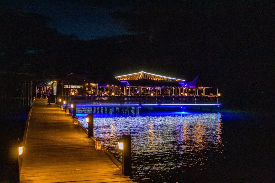 A long dock leading from Pinchos Grill & Bar, lit up at night, one of the best restaurants In Aruba for families.