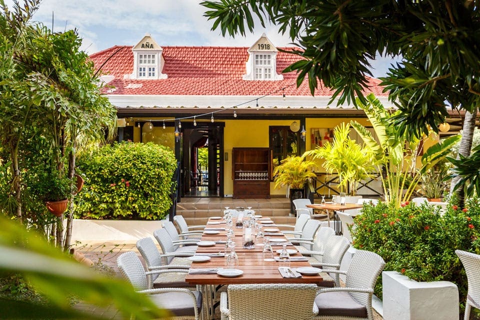 A long outdoor table, flanked by foliage, at Quinta del Carmen, one of the best restaurants In Aruba for families.