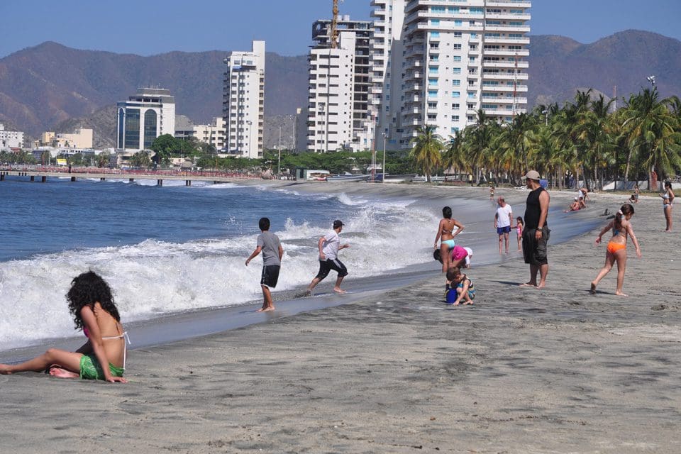 Several beach goers enjoy the sun and sand at Santa Marta, with large restort buildings in the background.