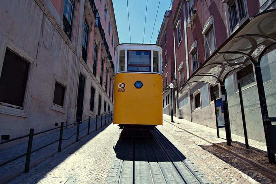 Tram 28, a yellow tram, races down a line in the city-center of Lisbon.