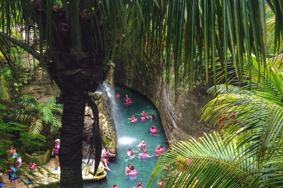Several pink tubes carrying people float down a clear blue river in a lush rainforest at Xcaret Eco Park, one of the best things to do in Playa del Carmen with kids.