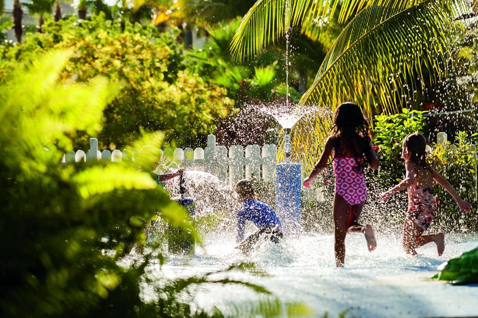 Three kids running and splashing in the on-site splash pad at The Ritz-Carlton, Grand Cayman.
