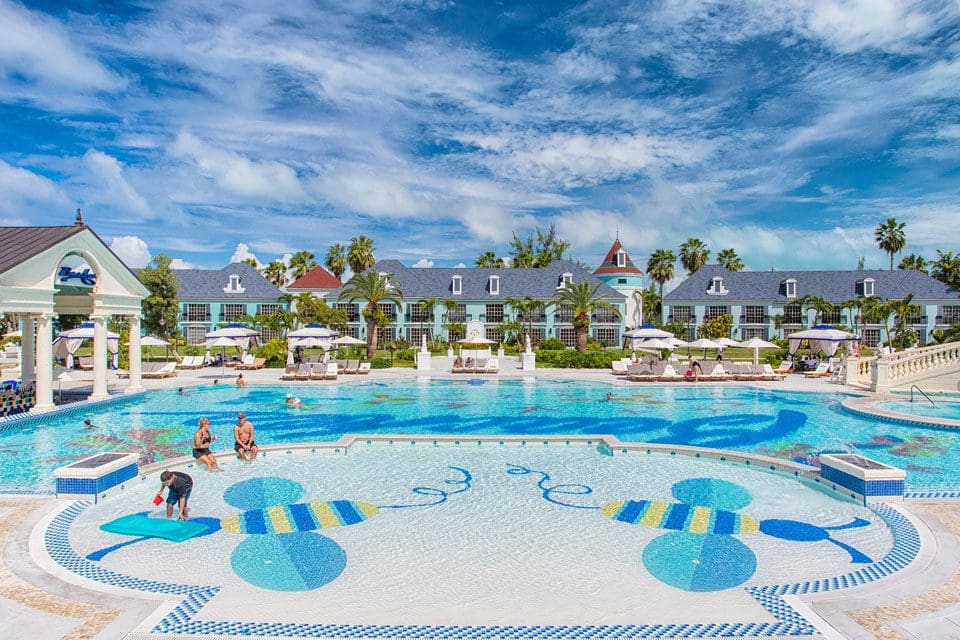 A pristine pool at  Beaches® Turks & Caicos Resort on a sunny day with a few families swimming in its shallow waters.