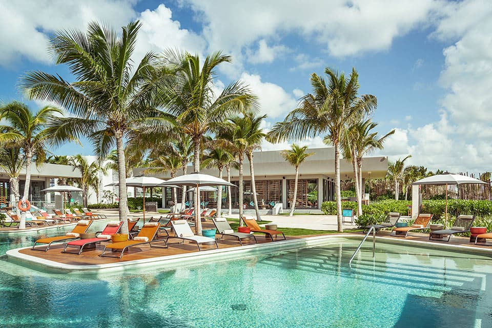 A stunning pool on-site at Andaz Mayakoba Resort, featuring colorful pool chairs and palm trees.