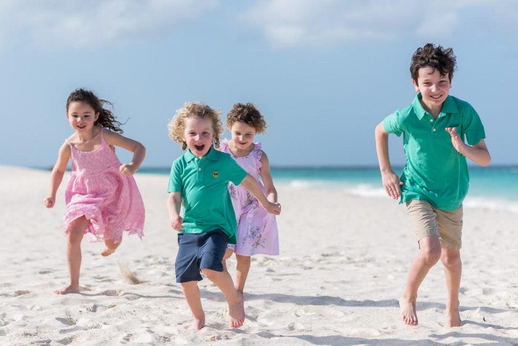 Four kids wearing brightly colored clothes run along a beach in Aruba, one of the best Thanksgiving destinations in the United States for families.