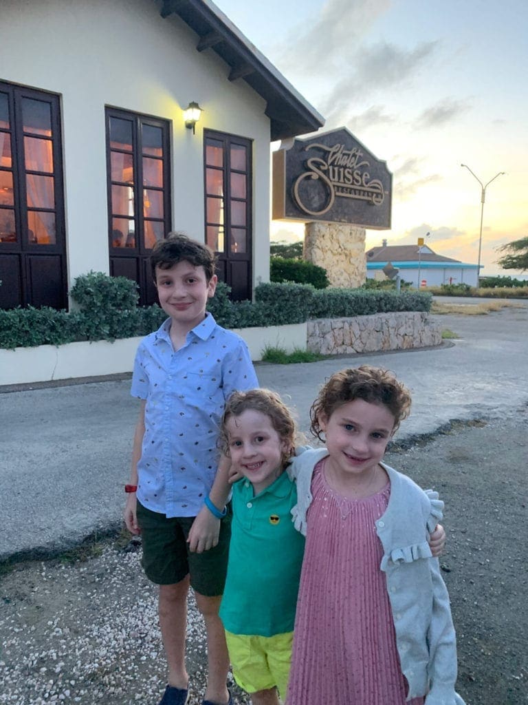 Three children smiling in front of Chalet Suisse, one of the best restaurants in Aruba for families. 