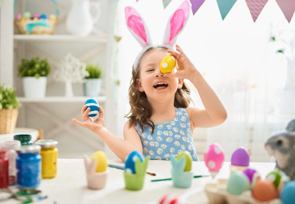 A young girl poses with her brightly colored Easter eggs, one blue with white stripes and one yellow with white polka dots. Dying eggs is a popular Easter tradition around the world.