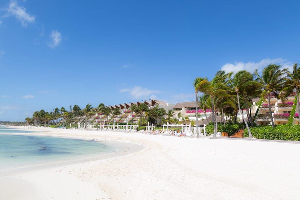 A stretch of white sand beach along the Riviera Maya, with resort buildings for Grand Velas Riviera Maya along the shore at one of the best all-inclusive resorts Playa del Carmen for families.