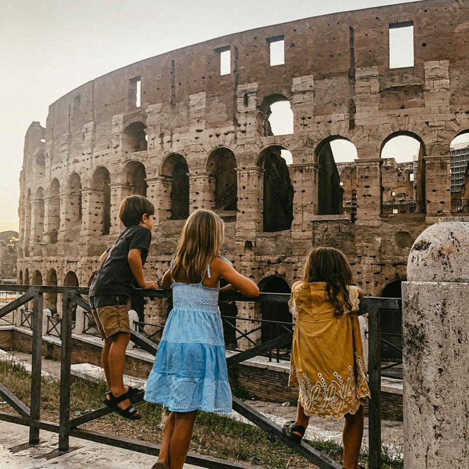 Three kids stand together, while looking at the Colosseum, a must stop on our Rome itinerary with kids.