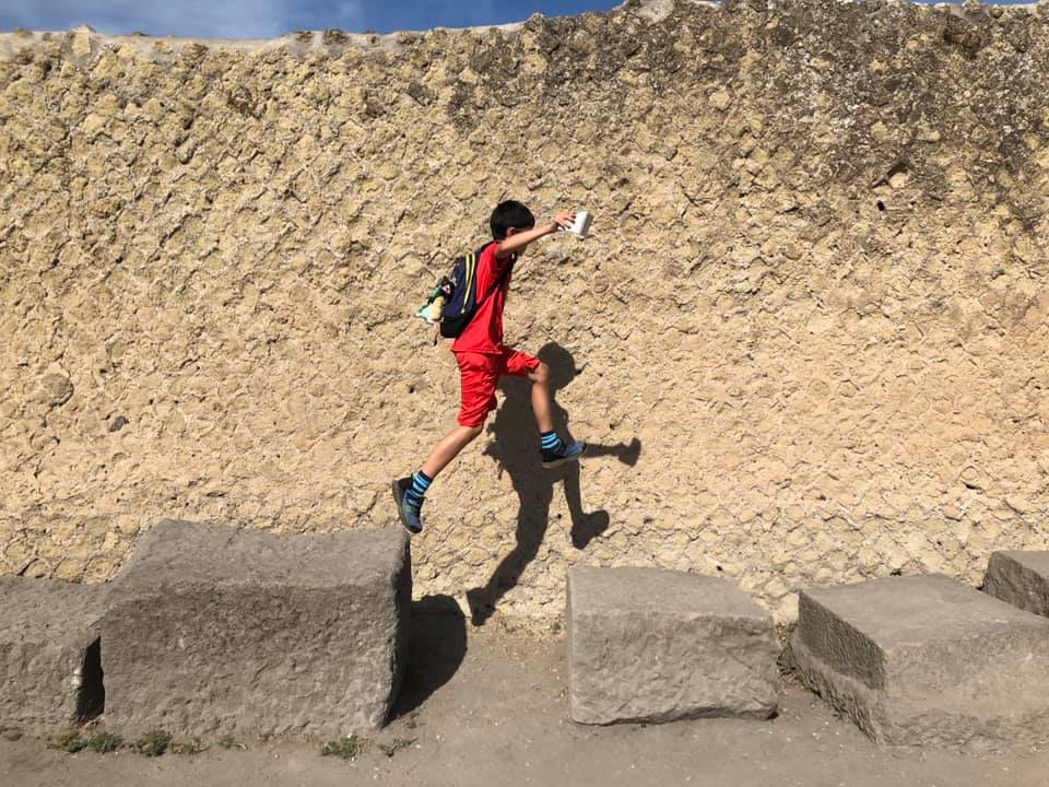 A young boy runs accross large stones within the grounds of Pompeii.
