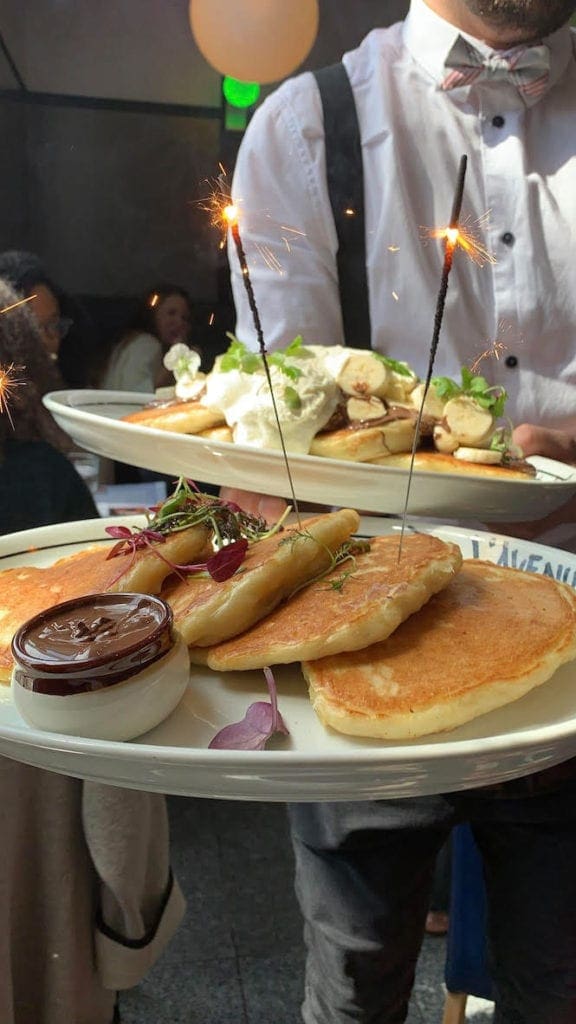 A waiter serves a delicious handful of food, including pancakes with sparklers, at a Montreal restaurant.