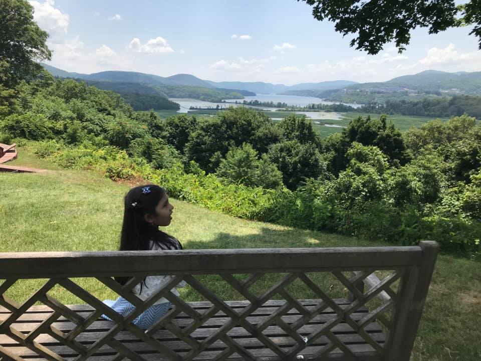 girl sitting on the bench facing the lake and the hills.