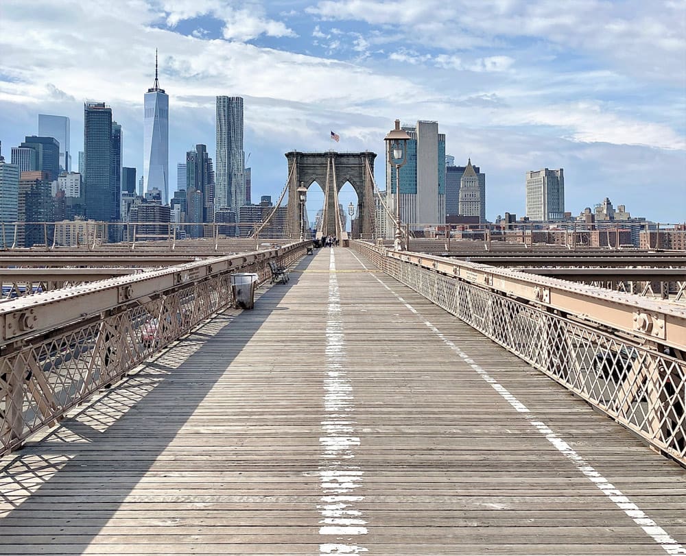 A view down the iconic Brooklyn Bridge on a sunny day, with the skyline of NYC in the distance, one of the best New York City outdoor activities for kids.