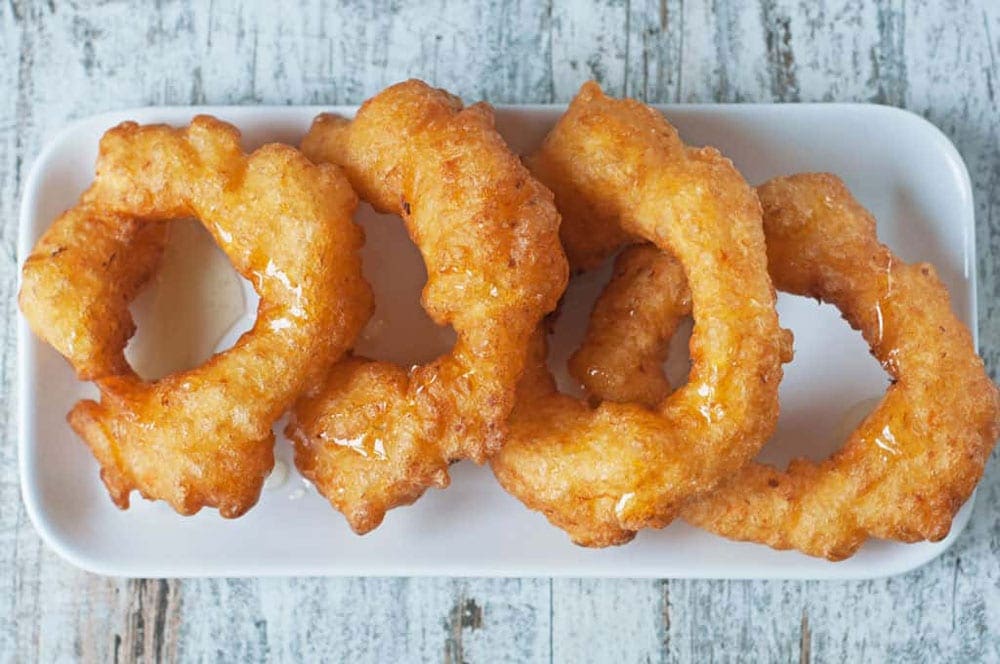 Four Peruvian picarones on a plate. Picarones look similar to old fashion donuts, a perfect treat as you take a virtual vacation from home to hike in Peru.