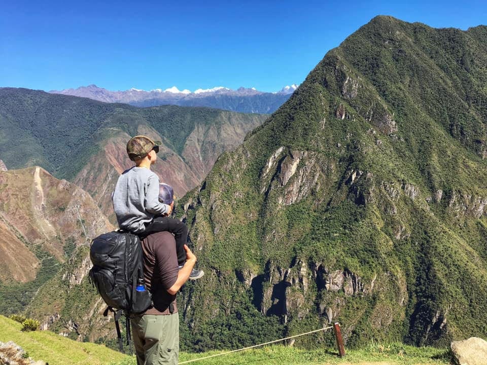 Son on the shoulders of his dad looking at a view of the Andes Mountains, one of the virtual hikes to enjoy on your virtual vacation from home to hike in Peru.