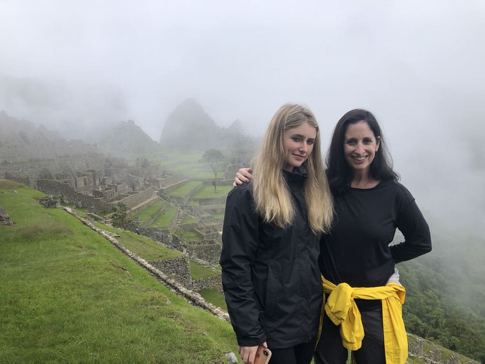 Mother and daughter stand in front of Peruvian ruins part of Machu Picchu.
