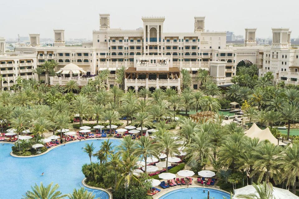 A full view of the resort buildings behind a large pool and swaying palms at the Jumeirah Al Qasr, one of the best family hotels in Dubai.