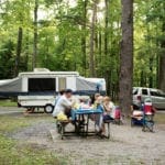 Family eating next to RV at a campsite with pop-up trailer