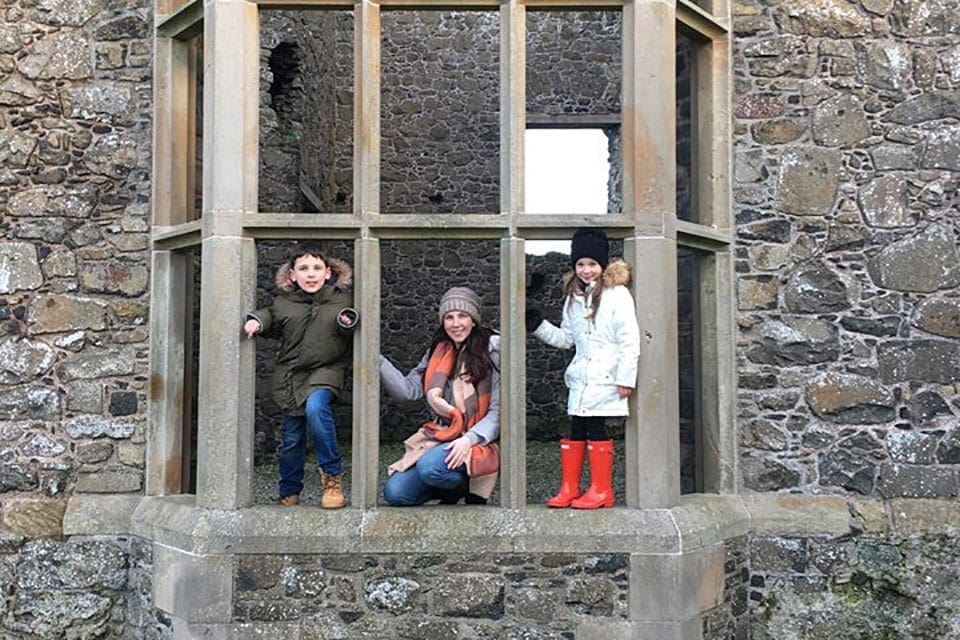 A mother and two kids stand within an old window on a castle. Seeing stunning castles is an importat part of our virtual vacation to Ireland.