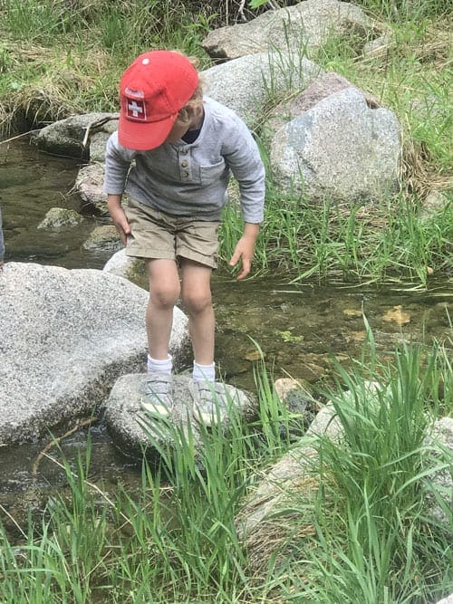 Small boy stands on a rock within a river while hiking near Denver.