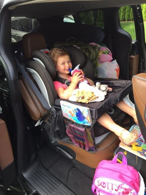 Young girl sits in car seat ready for a ride with her snacks and toys.