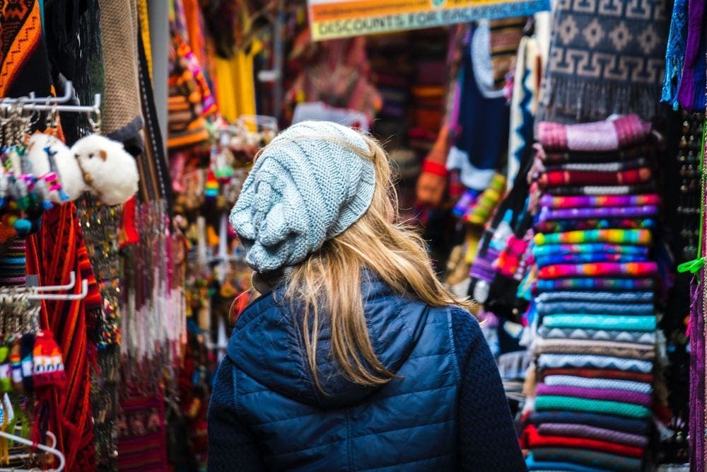 Woman explores market in Cusco, filled with things for sale like scarves, keychains, and clothing, the next stop on our Peru family vacation itinerary.