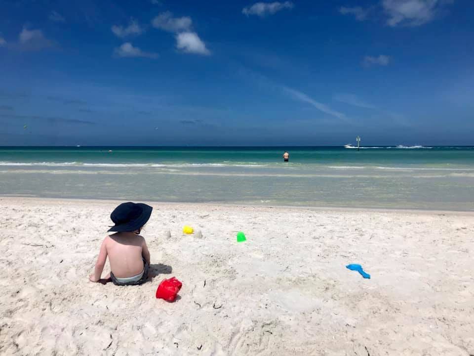 Toddler sits in the sand looking at the water off Clearwater Beach, one of the best Florida beaches for families.