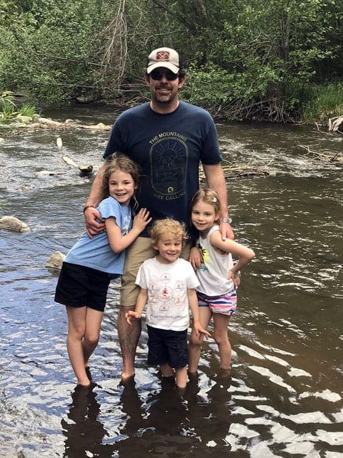 Family of four stand ankle deep in a river while hiking near Denver.